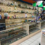 Glass wall display at Fox Plaza Smoke Shop featuring bongs, spoons, chillums, pipes, and one-hitters.