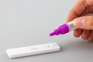 A hand squeezing reagent buffer drops onto the sample well of a white lateral-flow test cassette on a clean grey surface at El Paso Smoke Shops
