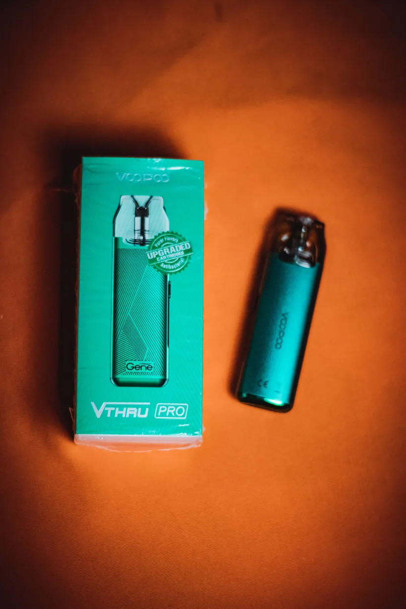Un solo vape desechable estilizado junto a su caja de venta sobre un fondo naranja en El Paso Smoke Shops