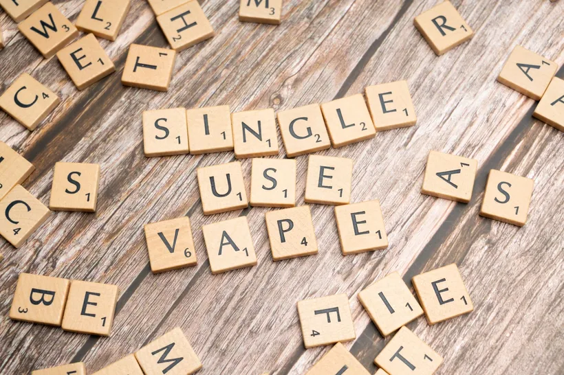 Fichas de Scrabble formando 'SINGLE USE VAPE' sobre madera desgastada en El Paso Smoke Shops