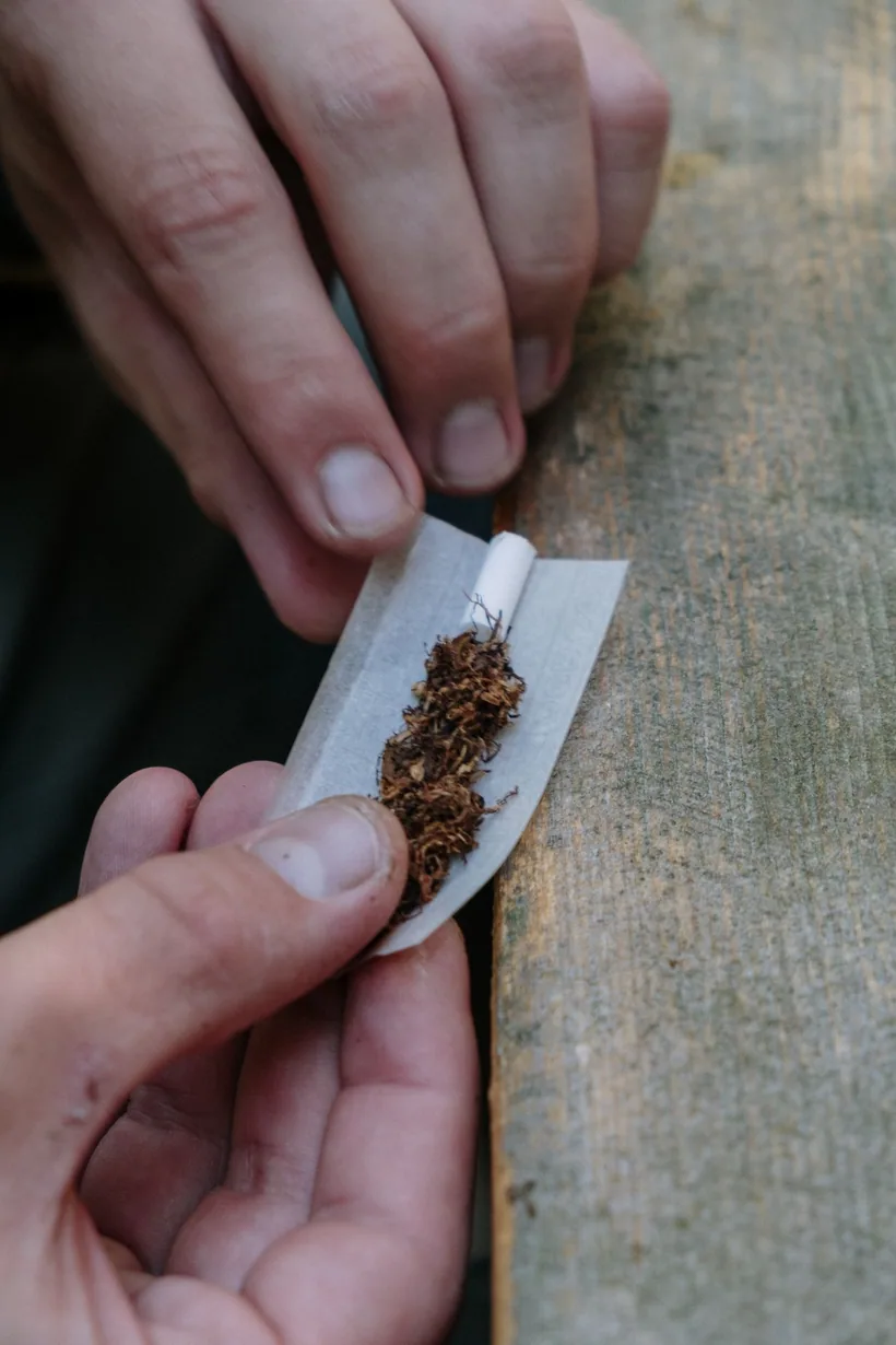 Hands placing a white filter tip and brown rolling tobacco onto a paper at El Paso Smoke Shops