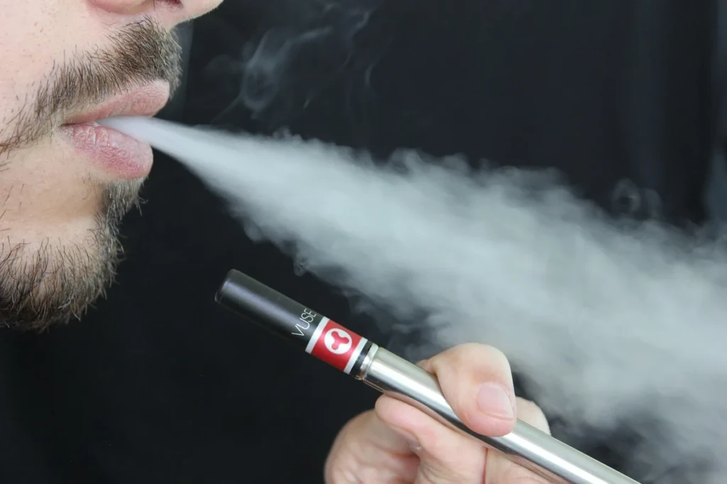 Adult exhaling vapor while holding a slim disposable-style vape e-cigarette at El Paso Smoke Shops