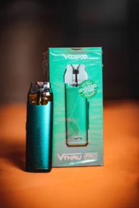 Teal pod-style disposable vape device standing beside its retail box under warm studio lighting at El Paso Smoke Shops