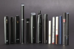 A studio lineup of more than a dozen disposable and pod vape devices arranged by size on a neutral gray background at El Paso Smoke Shops