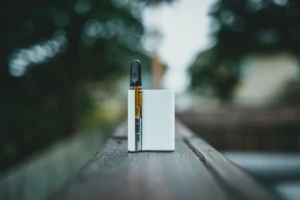 Close-up of a white pod-style disposable vape device resting on a wooden rail at El Paso Smoke Shops