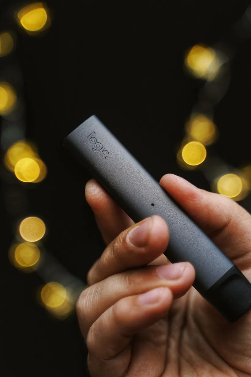 Adult hand holding a sleek sealed pod vape device against warm bokeh lights at El Paso Smoke Shops