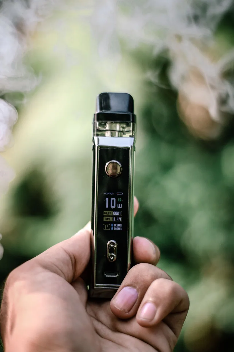 Hand holding a refillable pod vape whose display shows a live puff counter and wattage at El Paso Smoke Shops