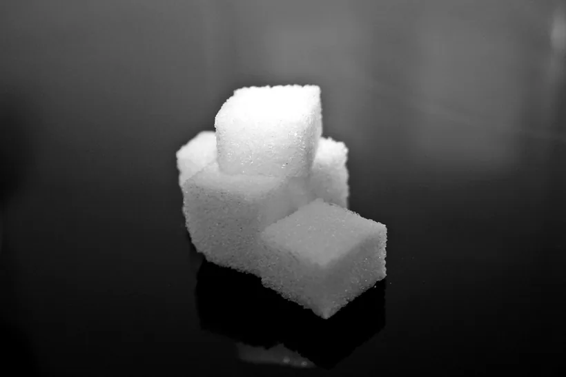A small stack of white sugar cubes on a dark reflective surface, illustrating the zero-sugar and sweetener discussion at El Paso Smoke Shops