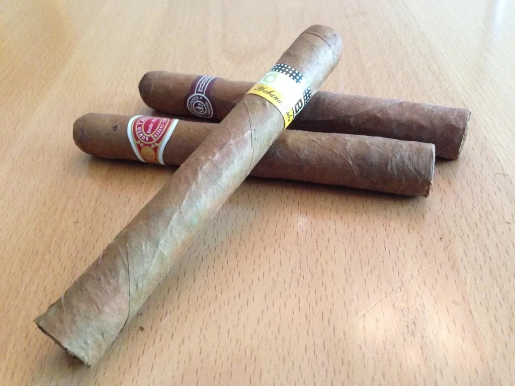 Three premium hand-rolled cigars with Montecristo and Romeo y Julieta bands resting on a wooden table at El Paso Smoke Shops