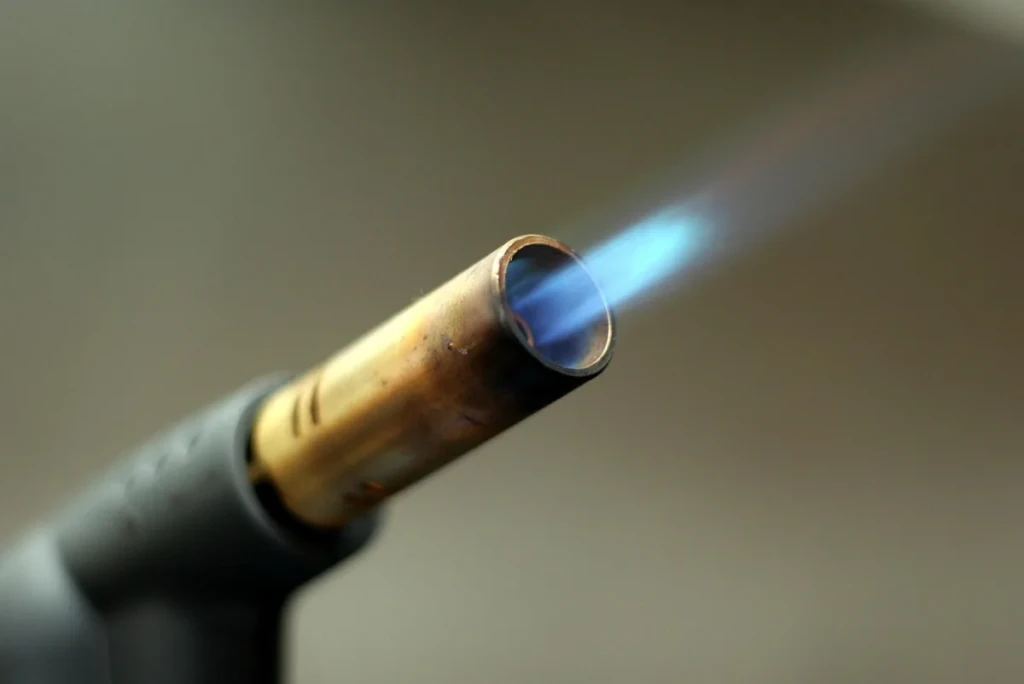 Handheld butane torch nozzle firing a focused blue jet flame at El Paso Smoke Shops