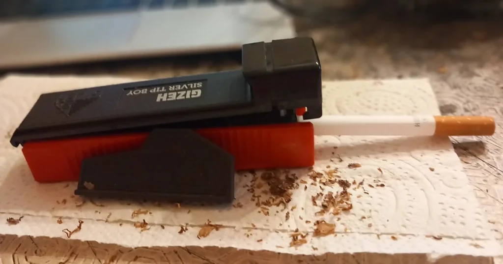 A black and orange cigarette rolling machine with a finished filtered cigarette and loose rolling tobacco beside it at El Paso Smoke Shops