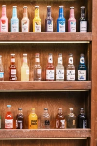 Wooden shelves lined with a colorful assortment of craft soda bottles in many fruit flavors at El Paso Smoke Shops