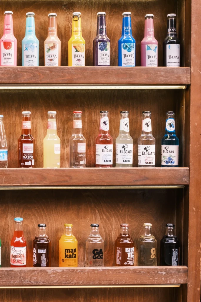 Wooden shelves lined with a colorful assortment of craft soda bottles in many fruit flavors at El Paso Smoke Shops