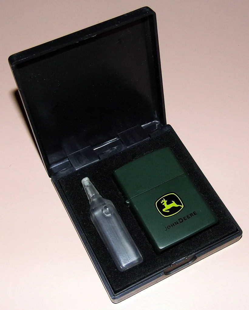 Un encendedor a prueba de viento Zippo verde junto a una botellita de líquido para encendedor en su estuche de presentación, en El Paso Smoke Shops