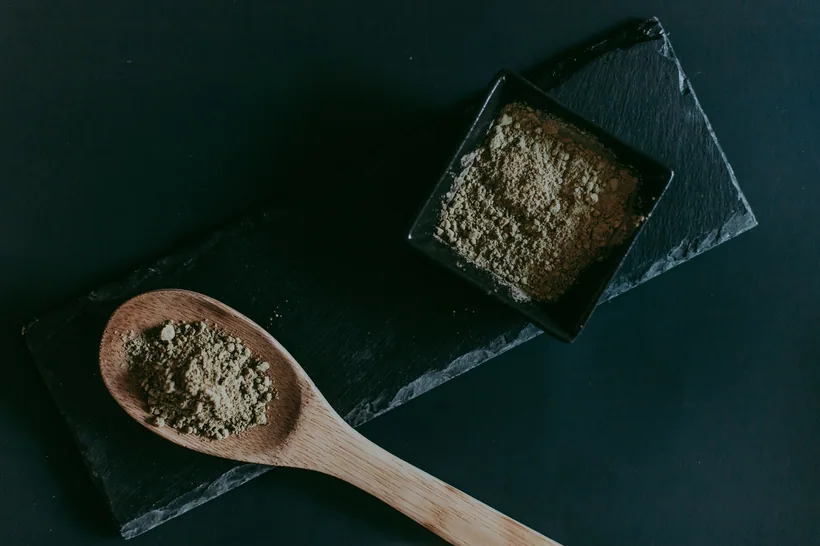 Tan ground kratom leaf powder on a wooden spoon and in a dish on dark slate at El Paso Smoke Shops