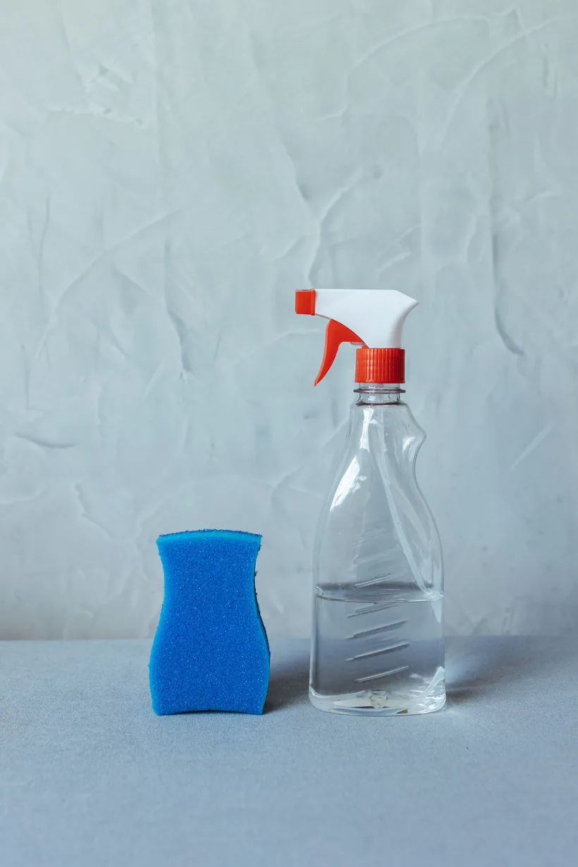 A clear trigger spray bottle of cleaning solution beside a scrubbing sponge at El Paso Smoke Shops