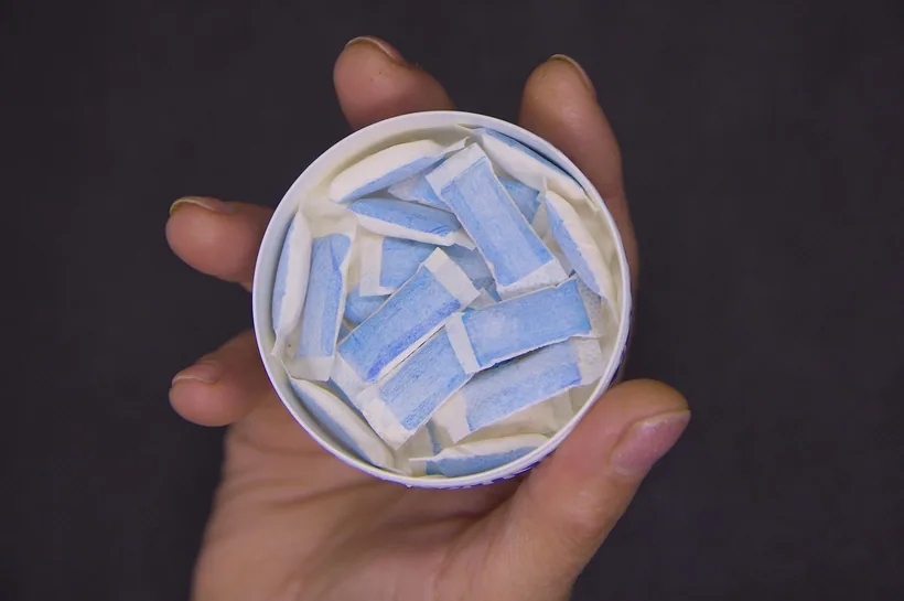 A hand holding an open can filled with white and blue oral nicotine pouches at El Paso Smoke Shops