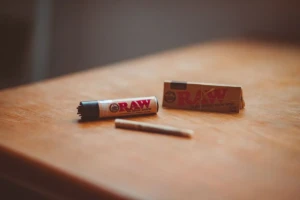 RAW natural rolling papers pack, an eco lighter, and a pre-rolled paper cone on a wooden table at El Paso Smoke Shops