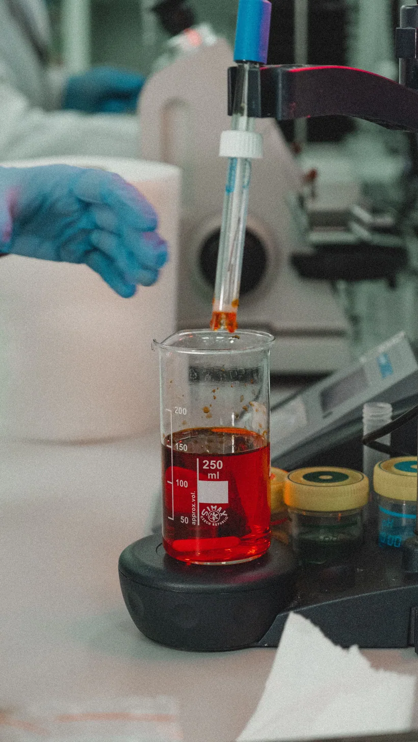 A vivid red chemical color reaction forming in a glass beaker as a dropper adds reagent in a lab at El Paso Smoke Shops