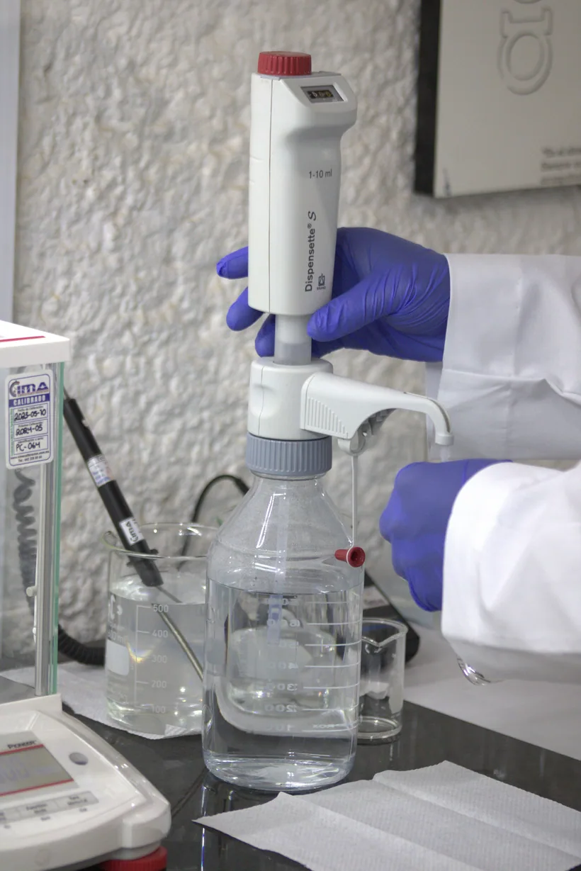 A gloved technician dispensing reagent testing fluid from a labeled bottle into glassware at El Paso Smoke Shops