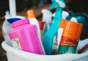 Bucket of assorted trigger spray bottles and odor-eliminating cleaning products, including a sprayer labeled for powerful cleaning action, at El Paso Smoke Shops