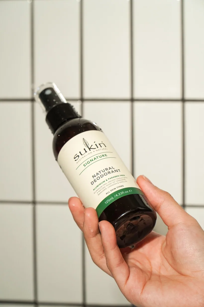 Hand holding an amber fine-mist odor-eliminating spray bottle against white tile at El Paso Smoke Shops