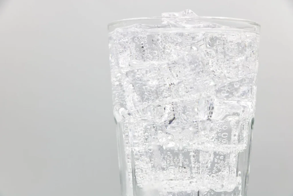 Tall glass of clear carbonated soda water filled with ice and rising bubbles on a clean studio background at El Paso Smoke Shops