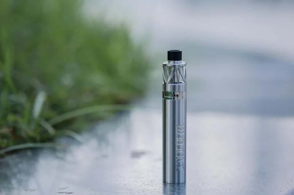 Sleek silver disposable-style vape pen device standing upright against green foliage at El Paso Smoke Shops
