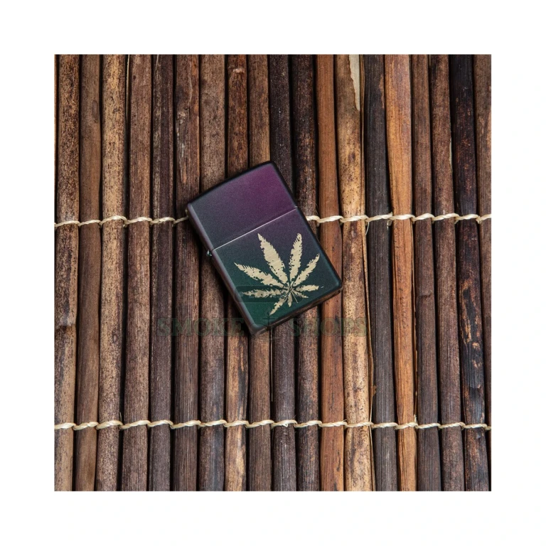 Close-up of the auto engraved marijuana leaf showing raw brass against the iridescent satin case on the Zippo 49185